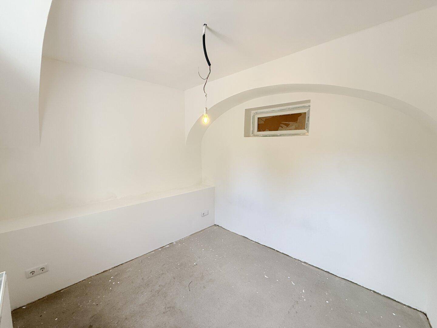 Leerer Raum mit Gewölbedecken, Betonboden und einem kleinen Fenster, wartet auf Fertigstellung.
