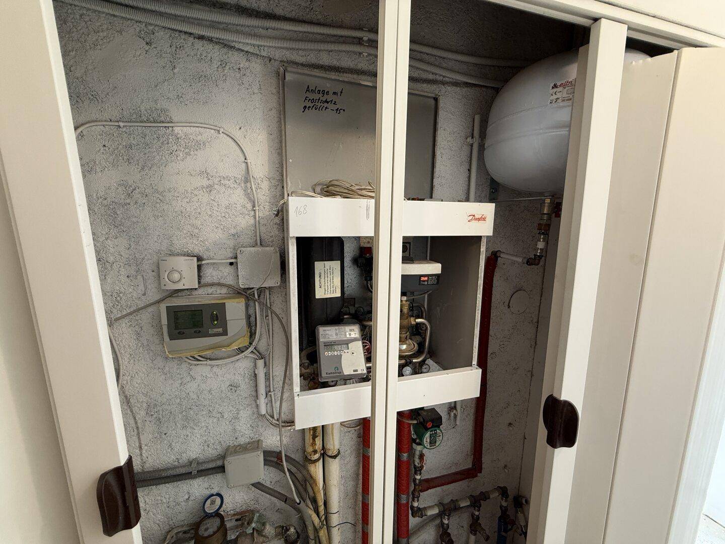 Technikraum mit Heizungsanlage, Rohren und Zählern, ordentlich in einem Schrank untergebracht.
