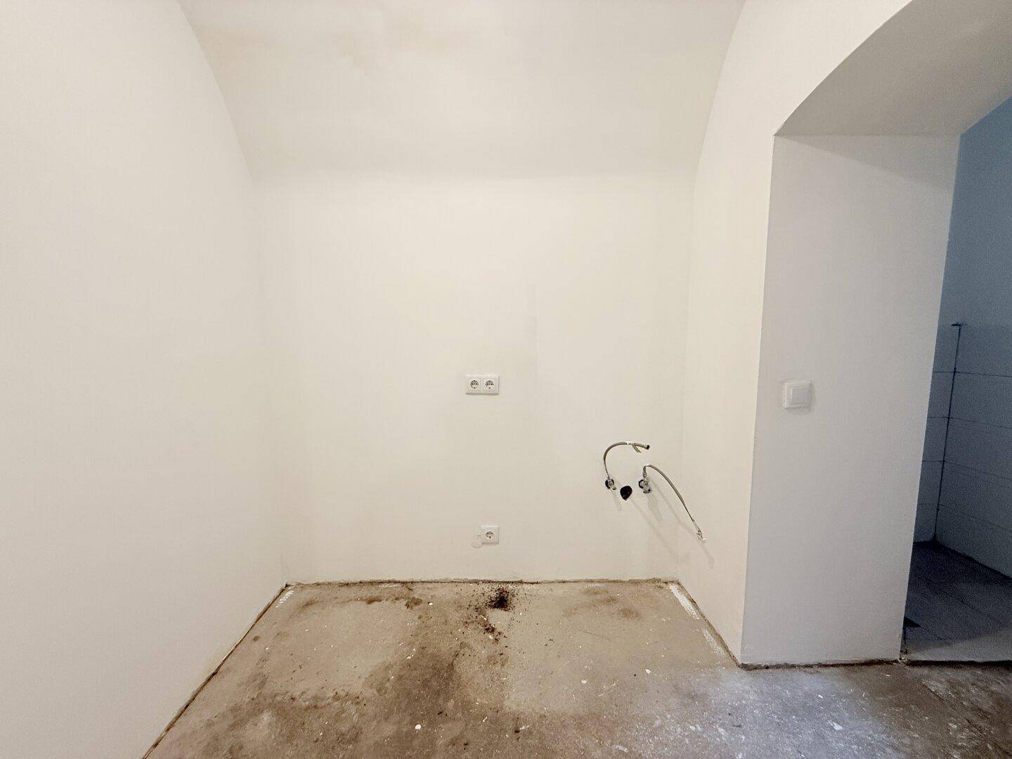 Unfertiger Küchenbereich mit Betonboden, Steckdosen und Anschlüssen für eine Spüle.