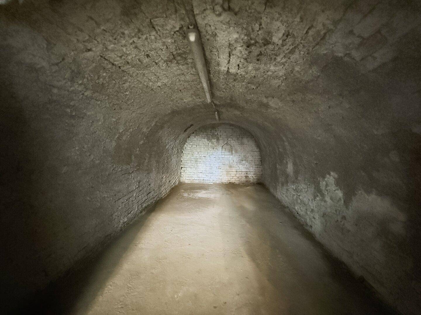 Ende des gewölbten Kellers mit rauen Steinwänden und einfacher Beleuchtung.