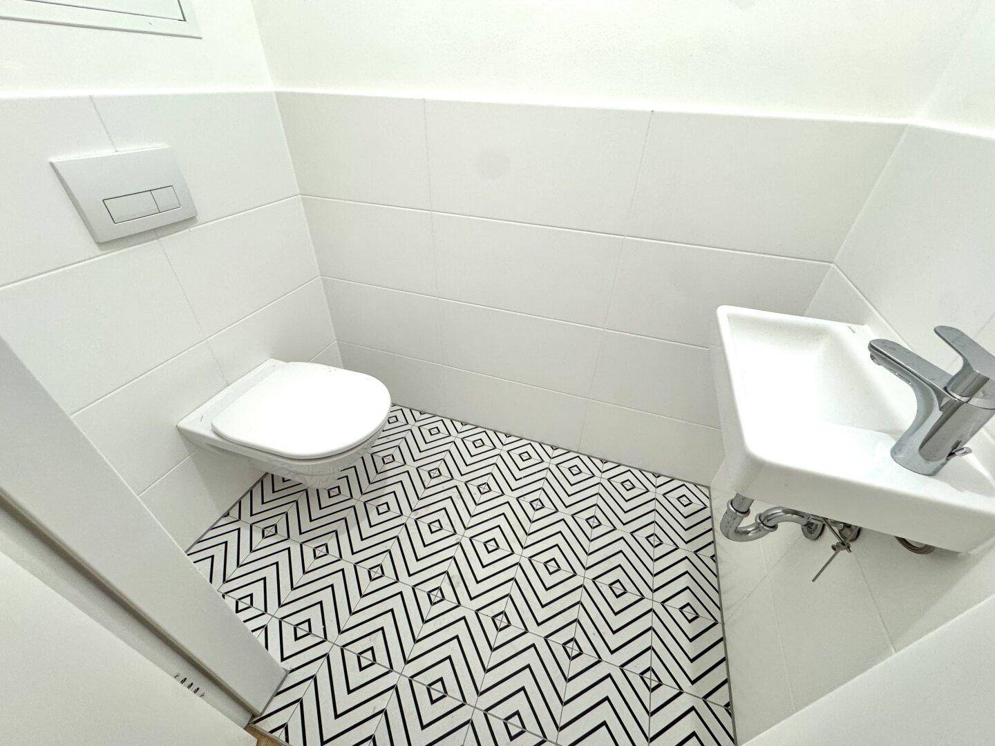 Modernes Gäste-WC mit auffälligem schwarz-weißem Fliesenmuster und wandhängendem WC.