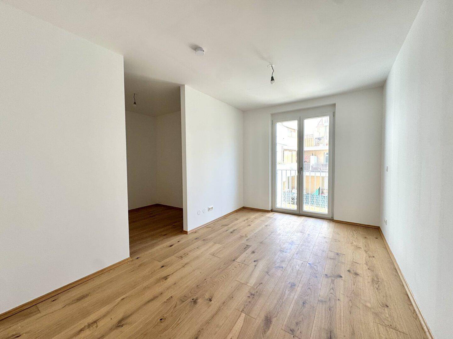 Helles Zimmer mit Eichenparkettboden, weißen Wänden und Zugang zu einem französischen Balkon.
