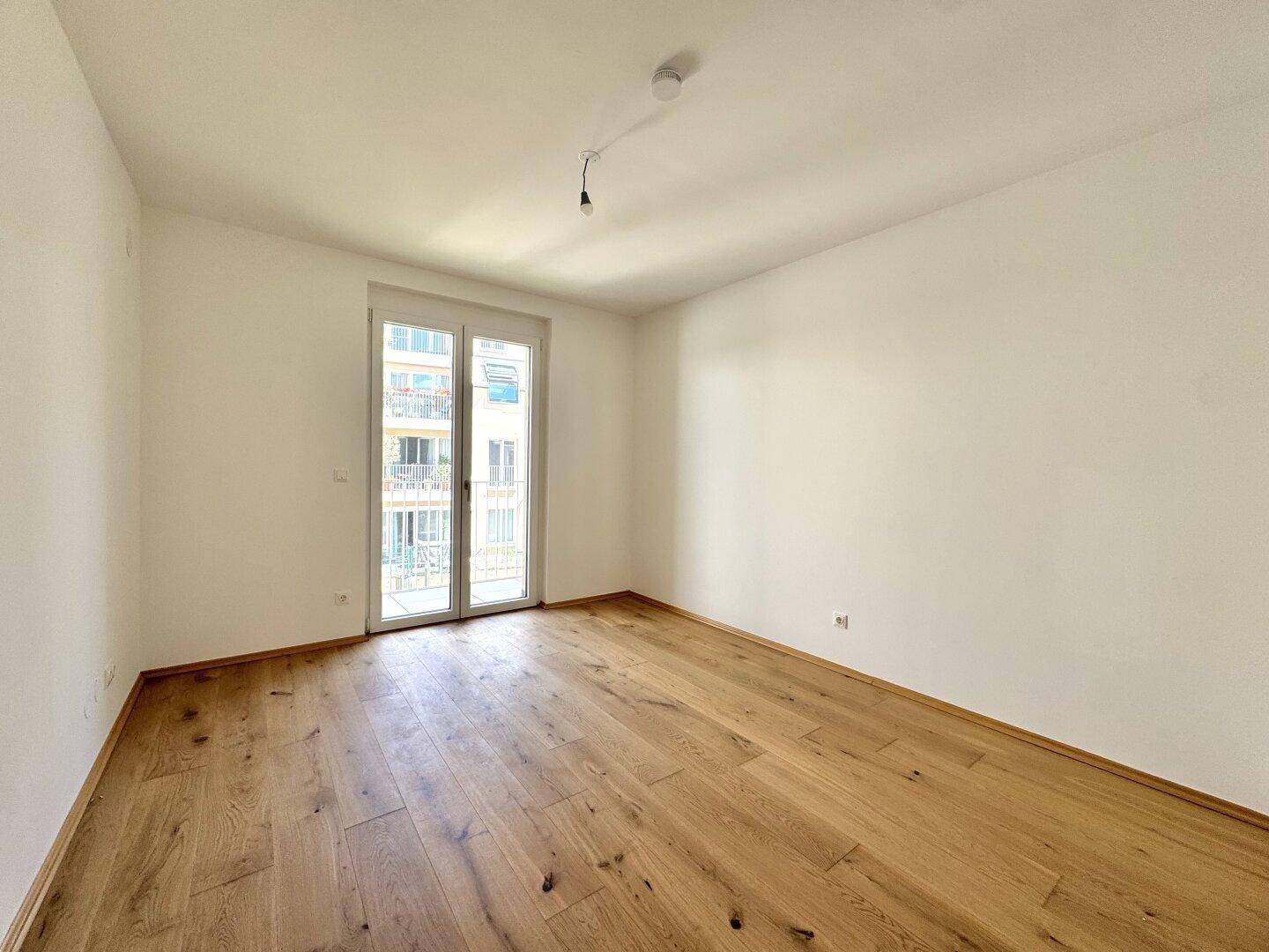 Geräumiges Schlafzimmer mit hellem Eichenparkettboden und einem französischen Balkon.