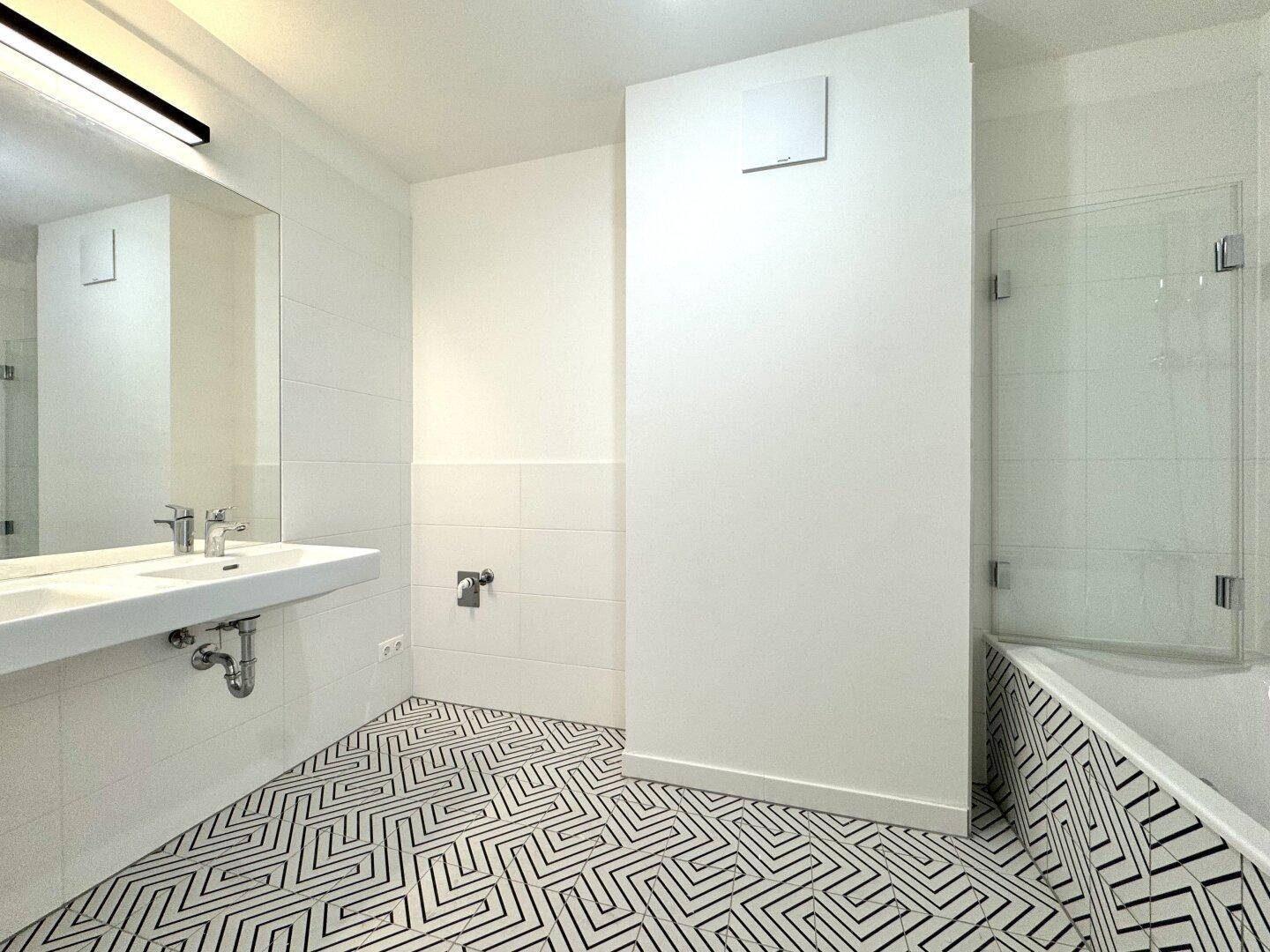Modernes Badezimmer mit Badewanne, begehbarer Dusche und stilvollen schwarz-weißen Bodenfliesen.