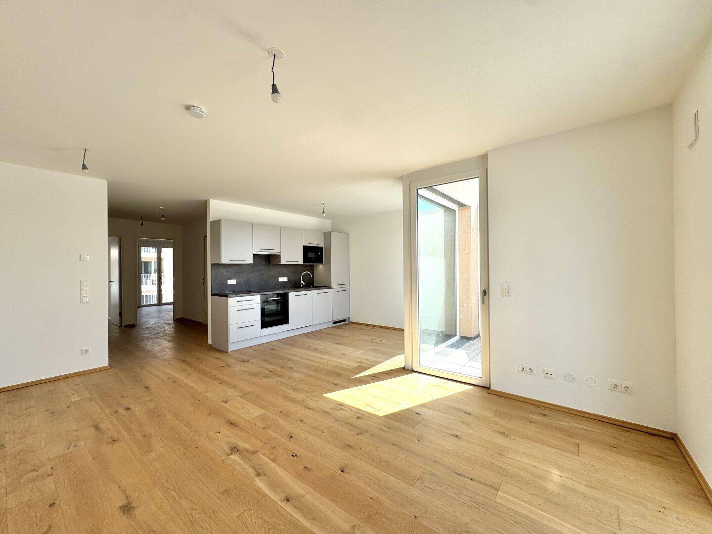 Offener Wohnbereich mit moderner Einbauküche, Eichenparkett und Balkonzugang.