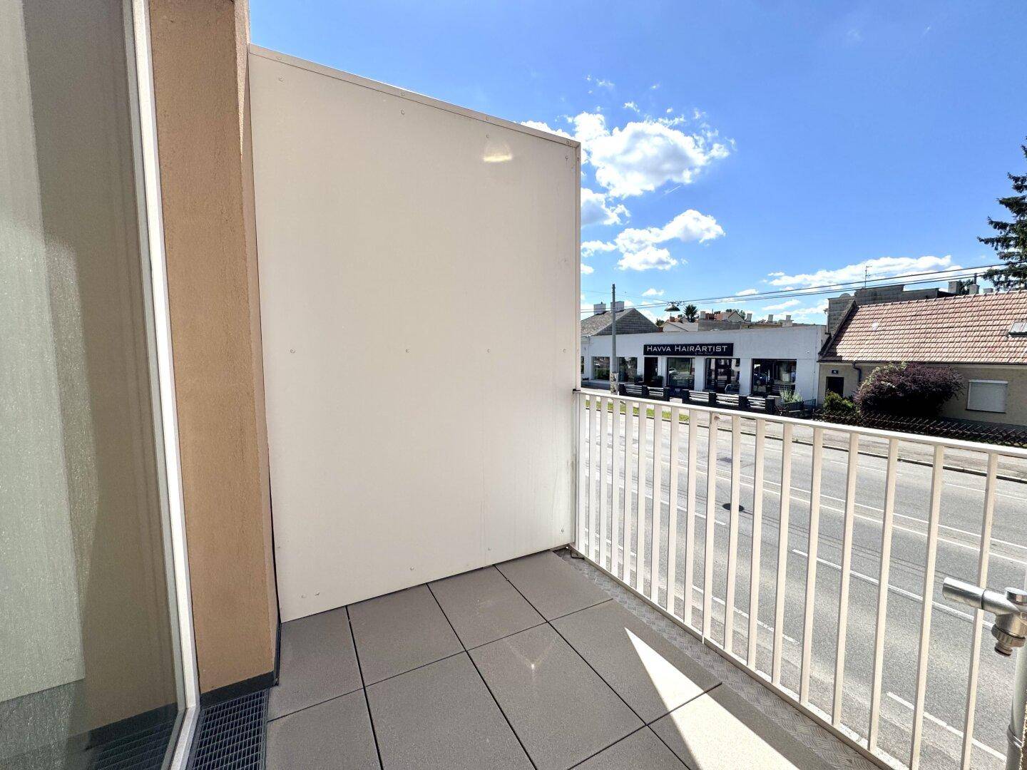 Balkon mit grauen Fliesen und Blick auf die Straße sowie gegenüberliegende Gebäude.