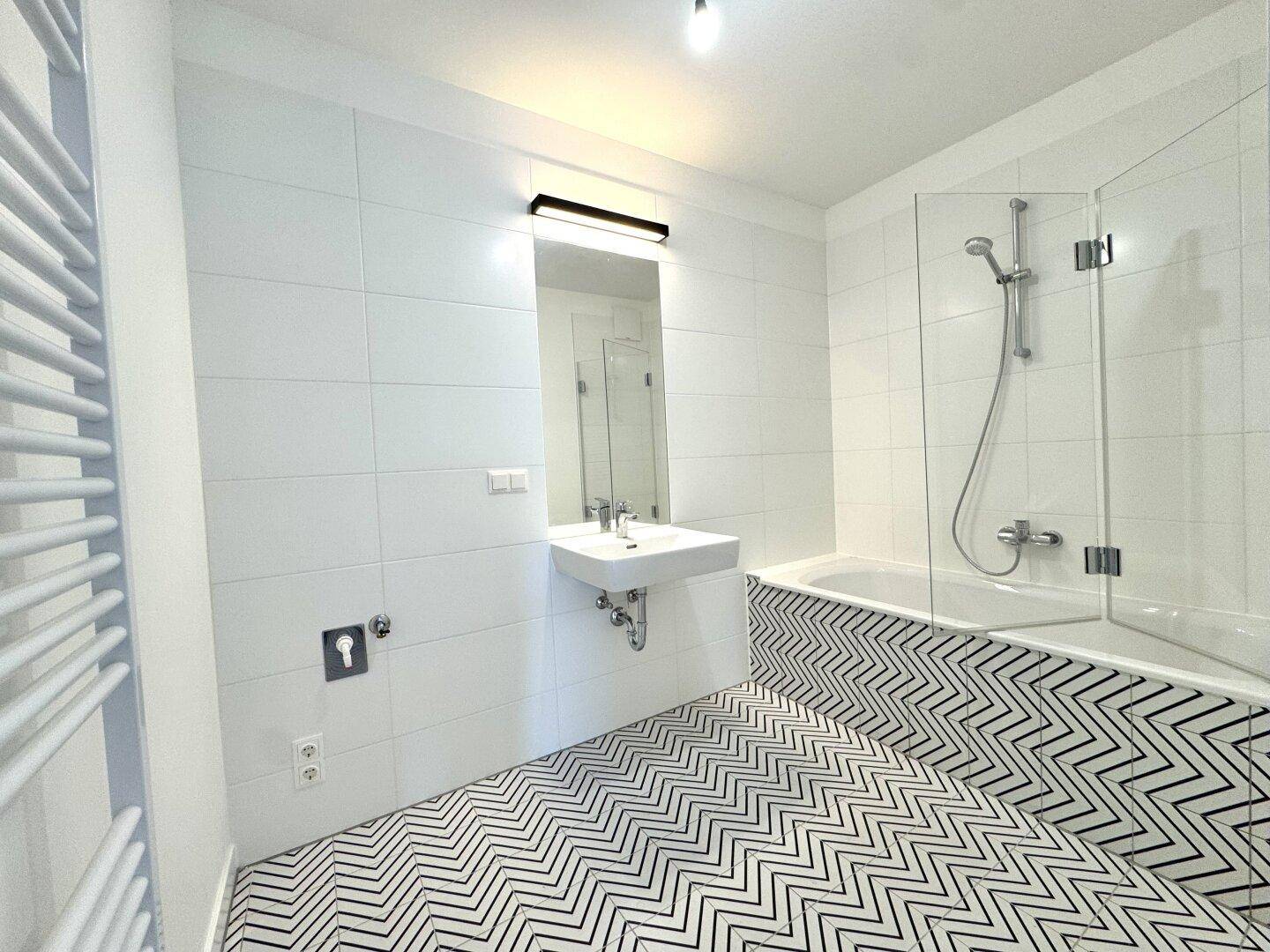 Modernes Badezimmer mit Badewanne, Dusche und auffälligem schwarz-weißem Fliesenboden.