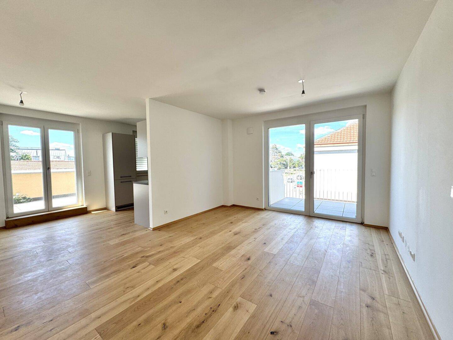 Heller Wohnbereich mit Holzboden, großen Fenstern und Zugang zu einem Balkon.