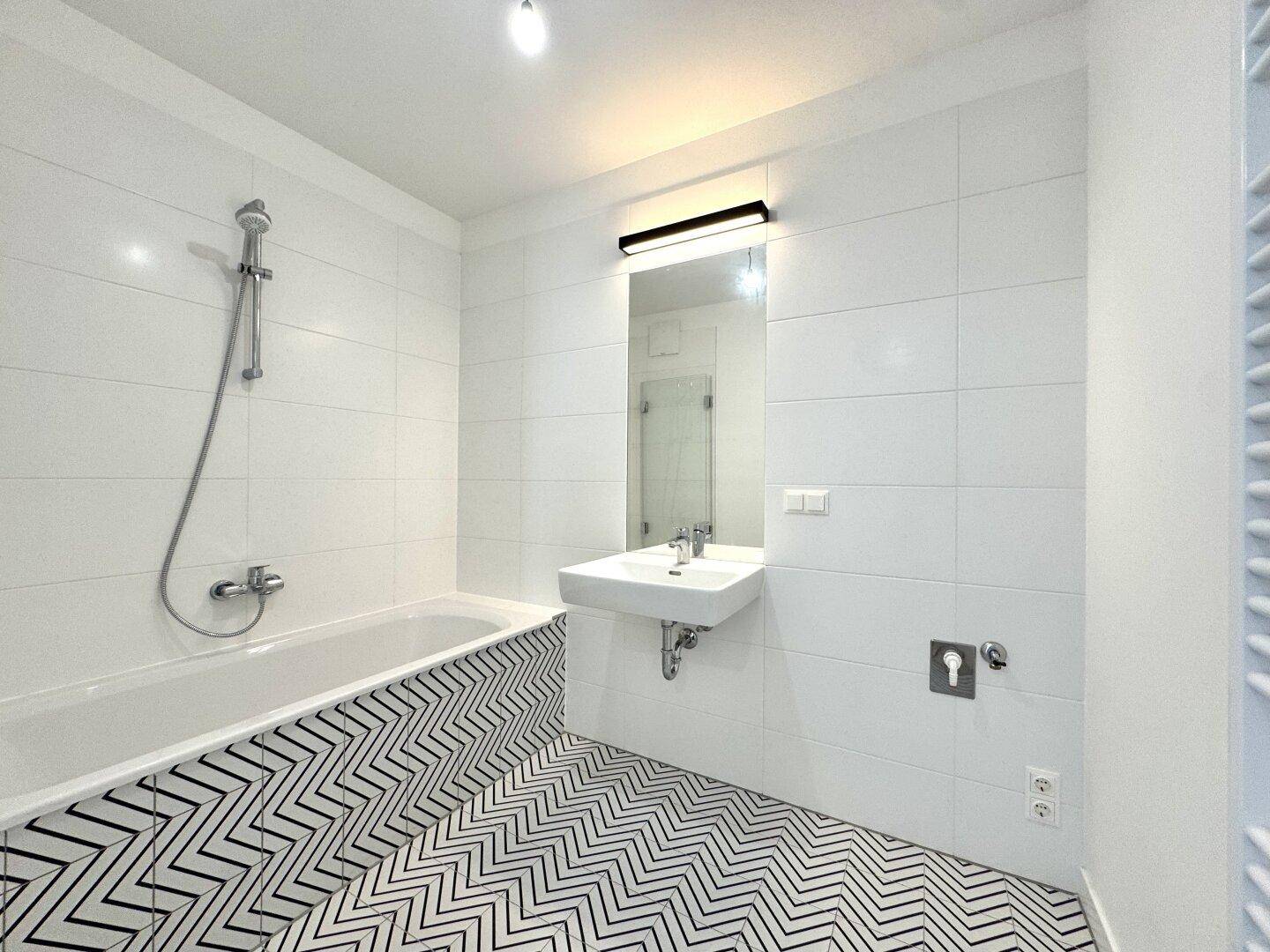 Modernes Badezimmer mit Badewanne, Waschbecken und auffälligen schwarz-weißen Fliesen.