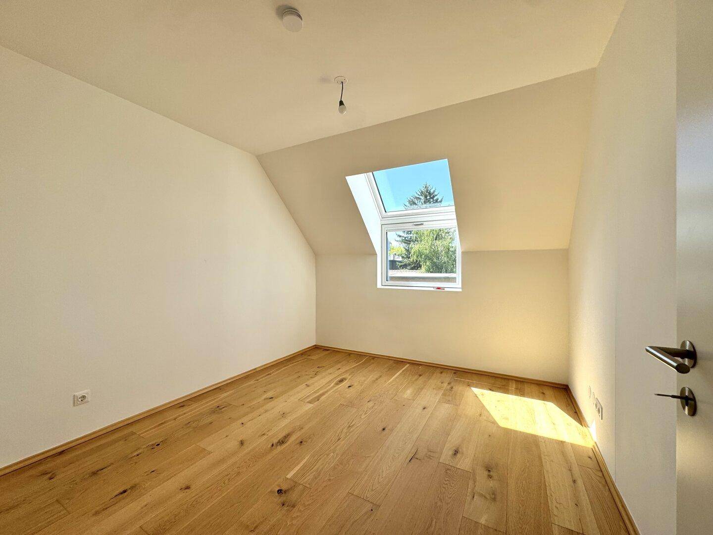 Helles Schlafzimmer im Dachgeschoss mit schrägen Wänden und einem großen Dachfenster.