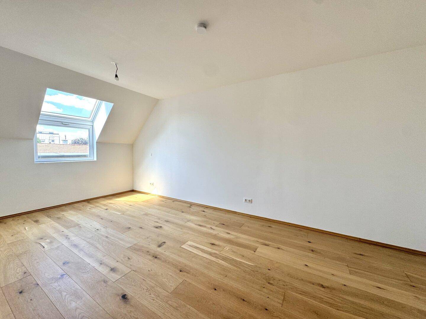 Geräumiges Schlafzimmer mit Holzboden und viel Tageslicht durch das Dachfenster.