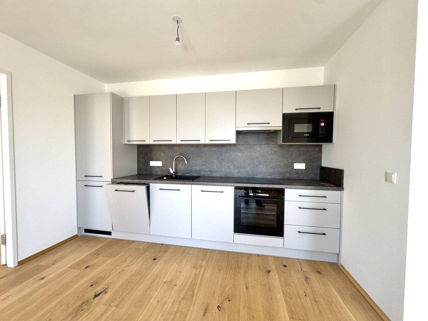 Moderne Einbauküche mit hellgrauen Schränken, dunkler Arbeitsplatte und integrierten Geräten.
