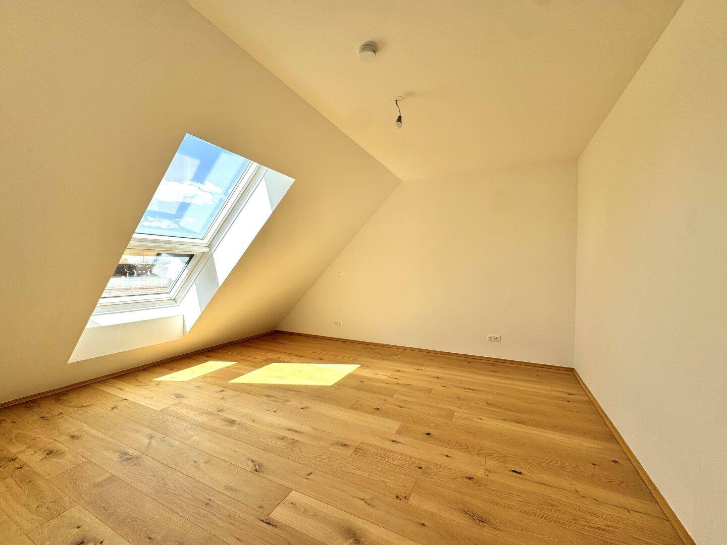 Schlafzimmer mit Holzboden, Dachschräge und einem großen Dachfenster.