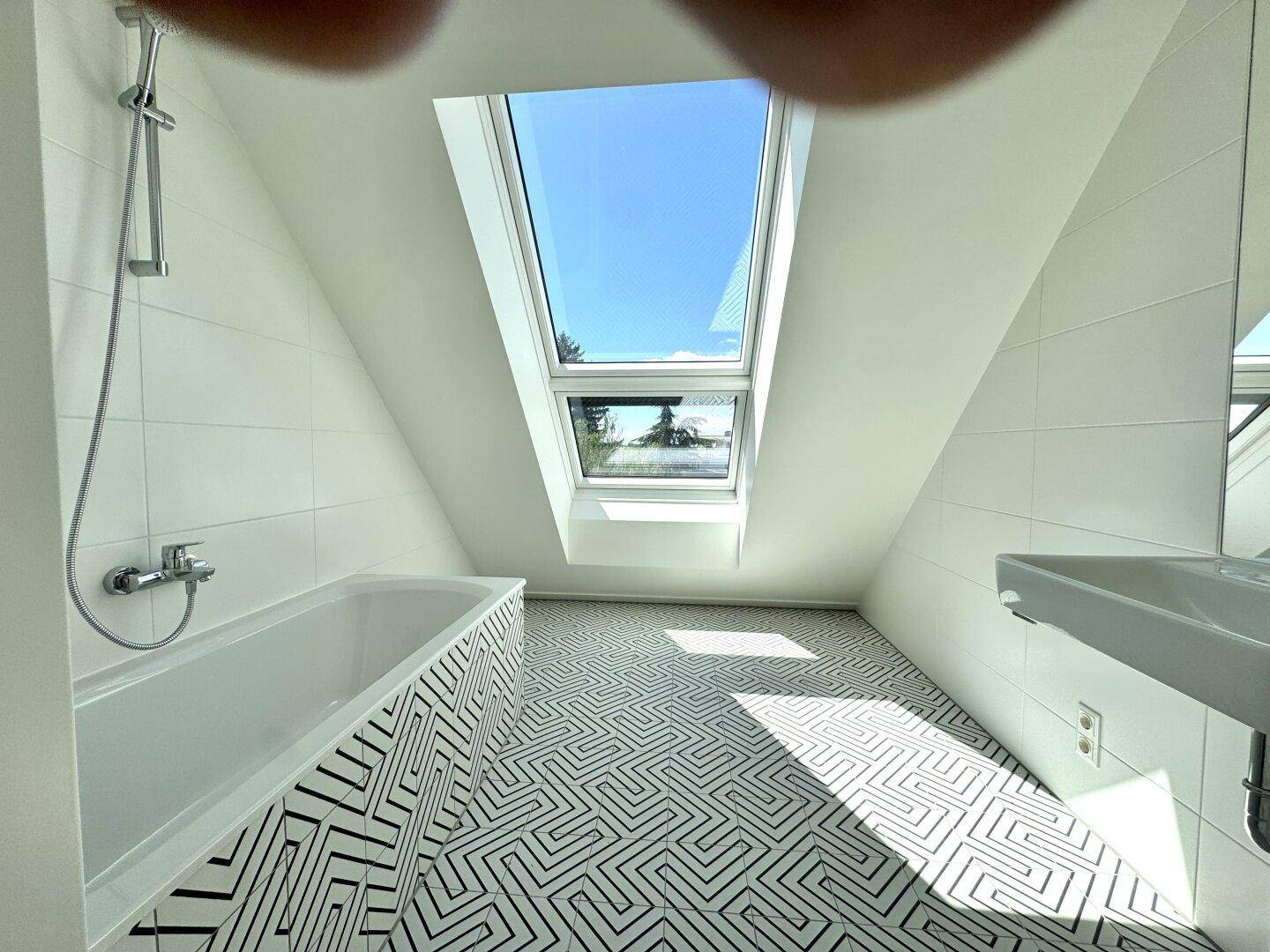 Modernes Badezimmer mit Badewanne, Dachfenster und auffälligen schwarz-weißen Fliesen.
