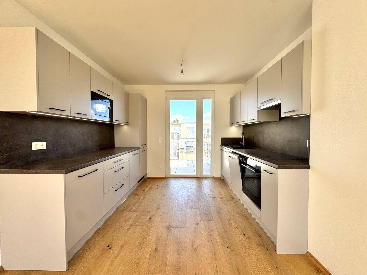 Moderne Küche mit hellgrauen Schränken, dunkler Arbeitsplatte und Zugang zum Balkon.