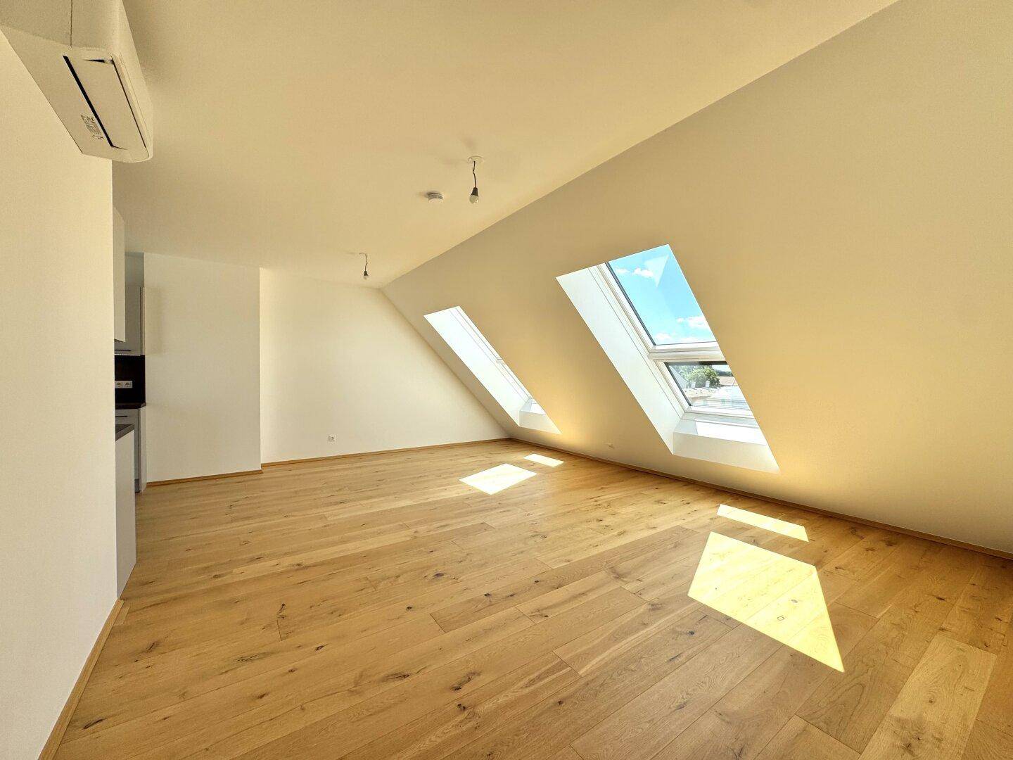 Heller Raum mit Holzboden, Dachschrägen und großen Dachfenstern für viel Tageslicht.