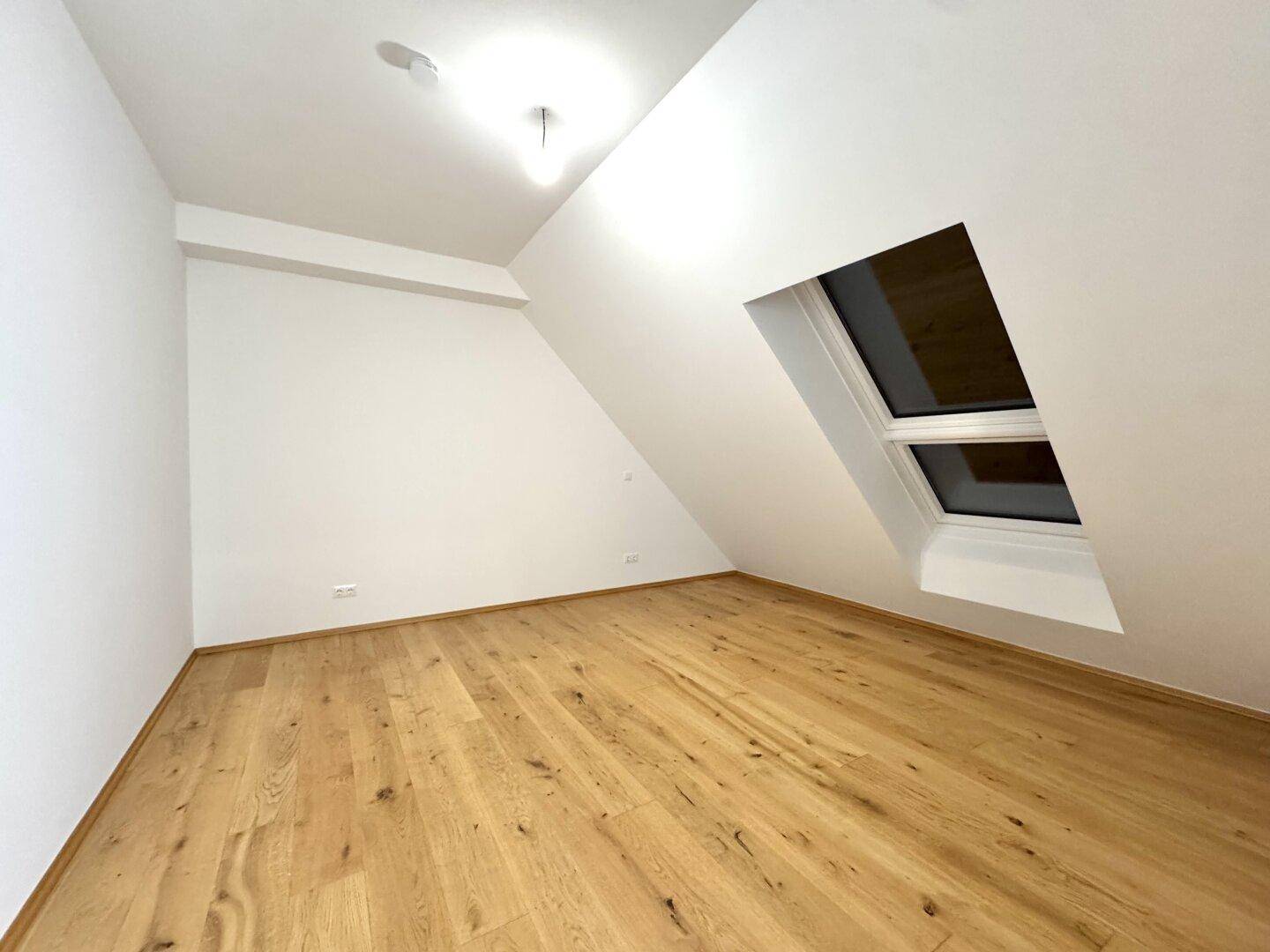 Heller Raum mit Holzboden, weiß gestrichenen Wänden und einem Dachfenster.