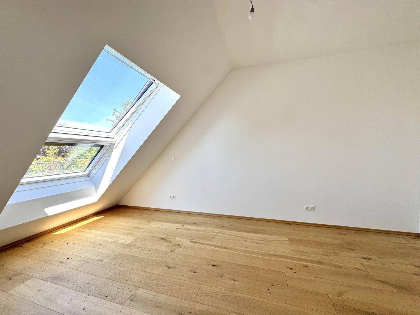 Lichtdurchflutetes Zimmer mit großem Dachfenster und hellem Holzparkettboden.