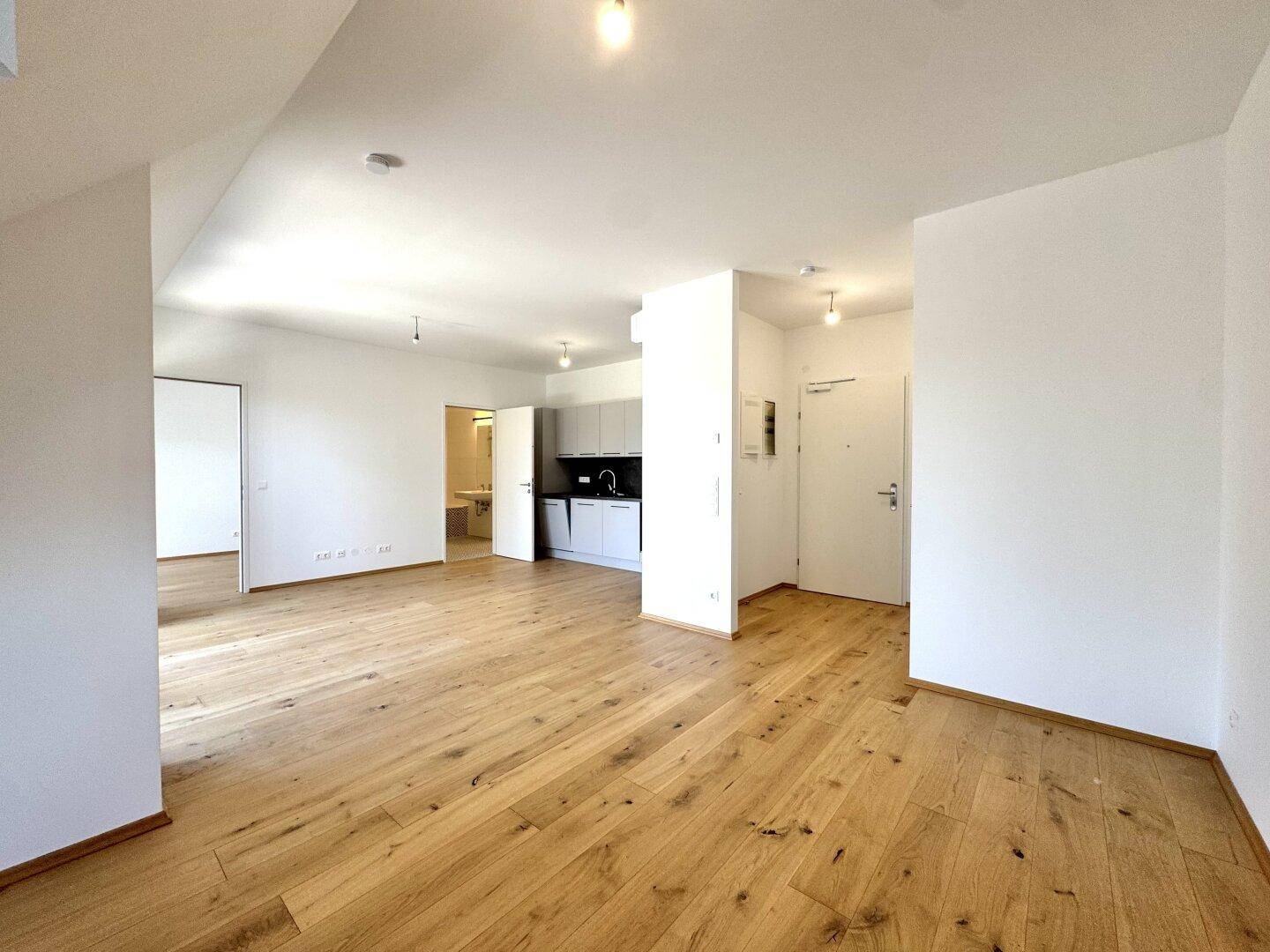 Geräumiger offener Wohnbereich mit hellem Holzparkett und Blick zur modernen Küche.