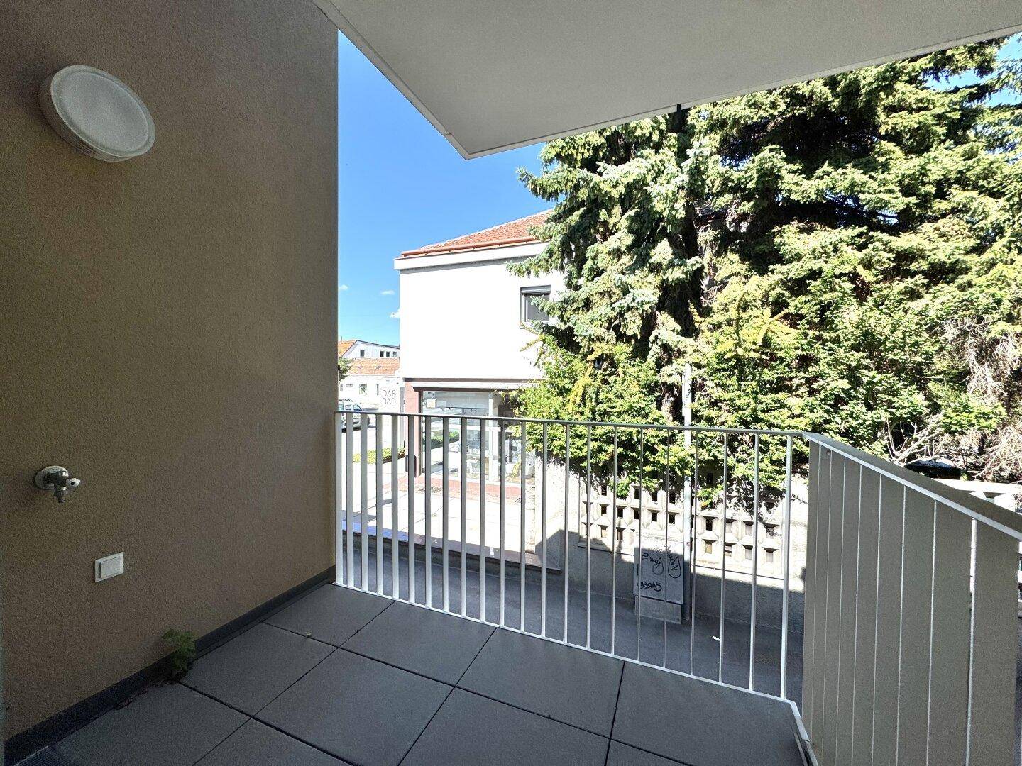 Heller Balkon mit Fliesenboden und Blick ins Grüne sowie auf die umliegenden Gebäude.