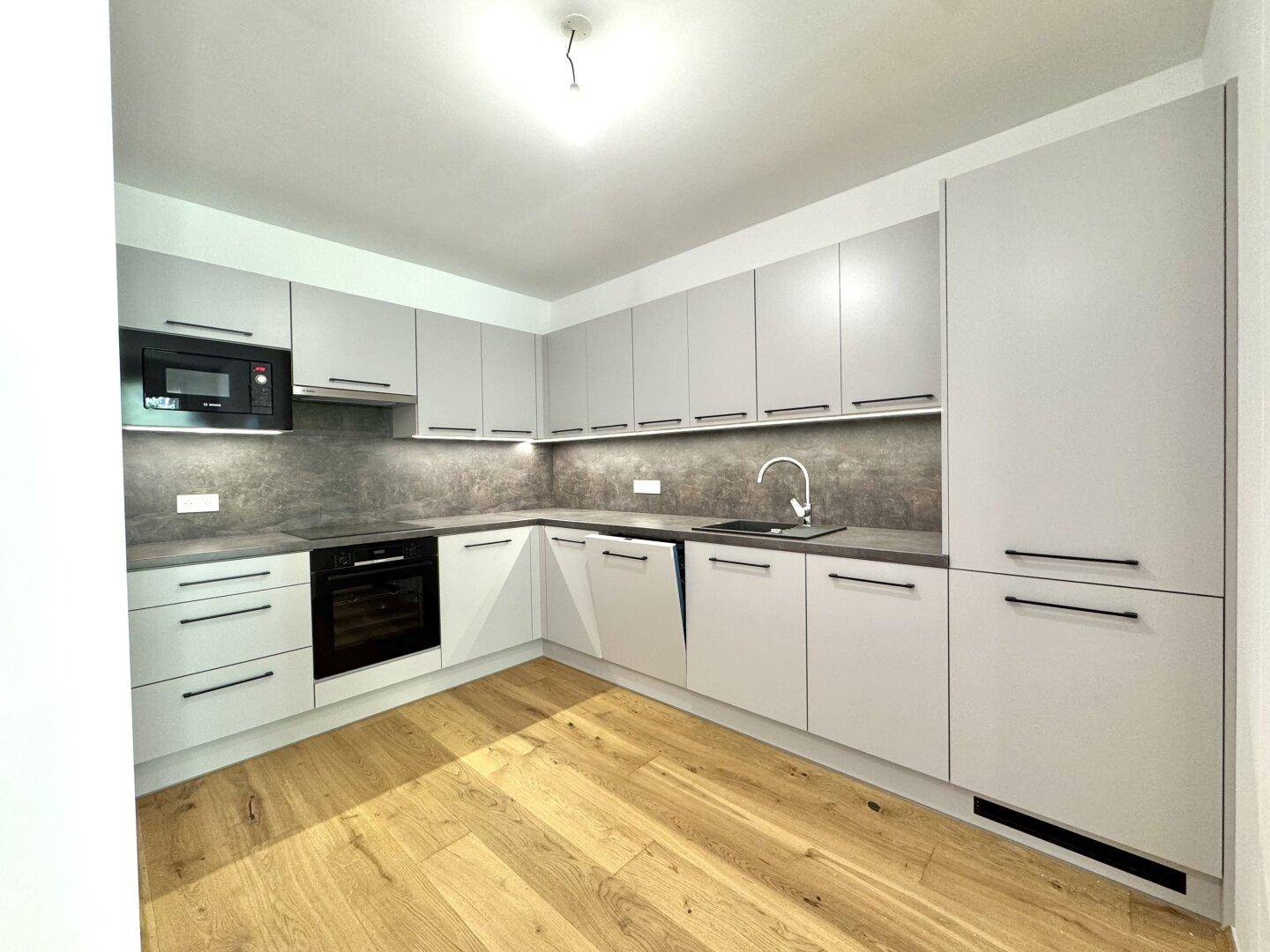 Moderne Einbauküche mit hellgrauen Fronten, integrierten Geräten und Holzboden.