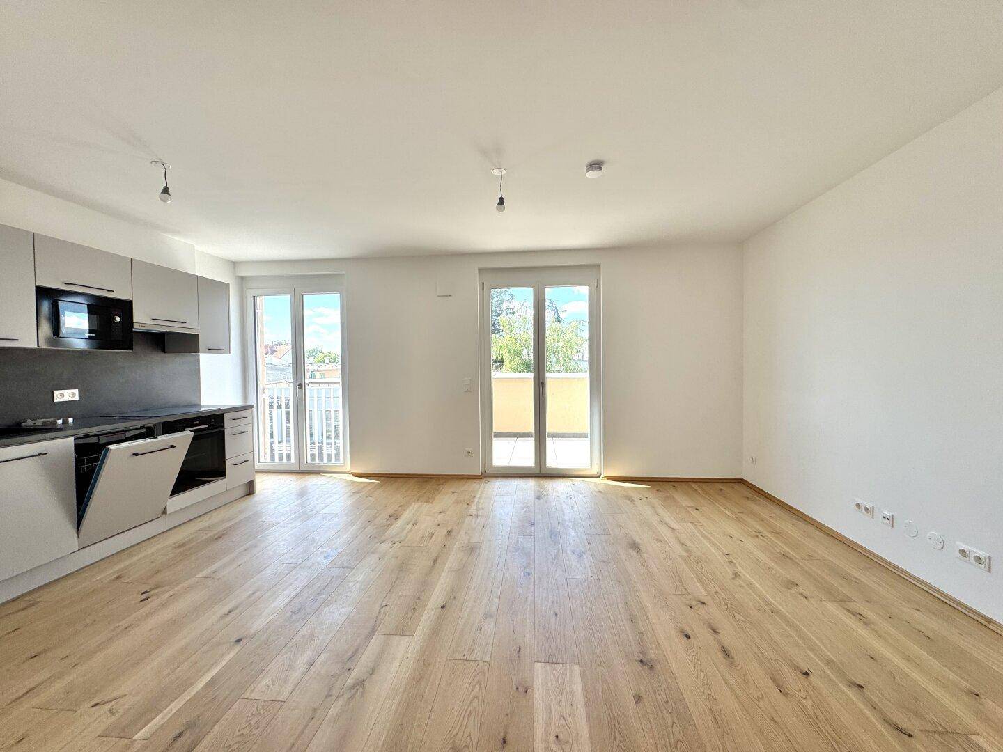 Heller offener Wohn- und Küchenbereich mit Eichenparkett und Zugang zu einem Balkon.
