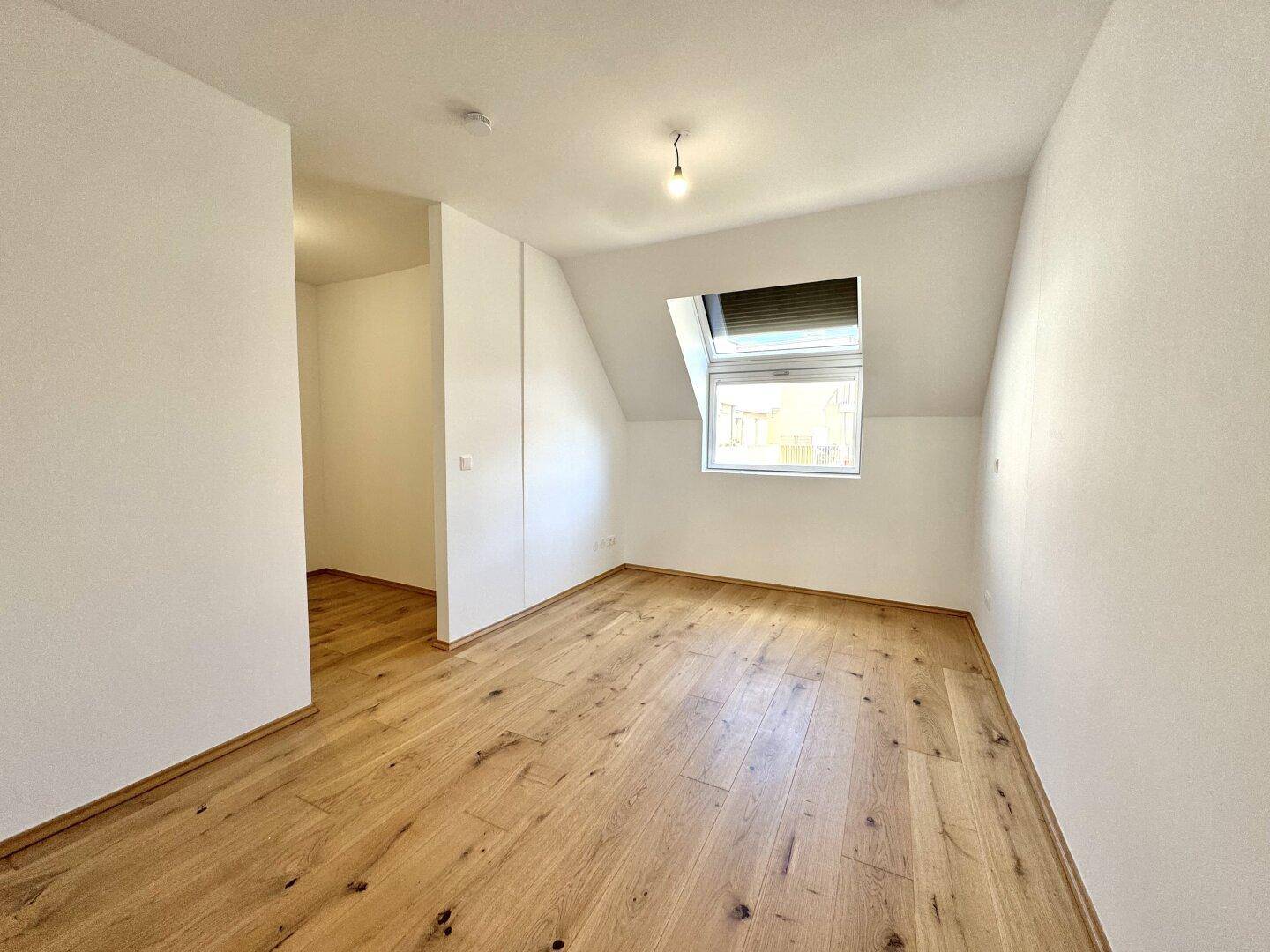 Helles Schlafzimmer im Dachgeschoss mit Holzboden und Dachfenster, ideal für ein gemütliches Ambiente.