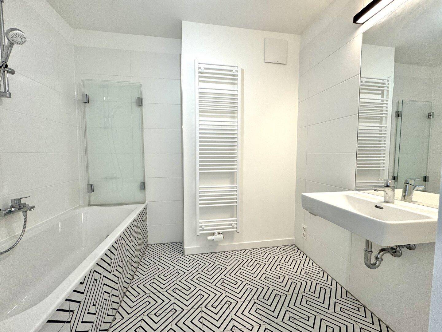 Modernes Badezimmer mit geometrischen Fliesen, Badewanne, Dusche und beheiztem Handtuchhalter.