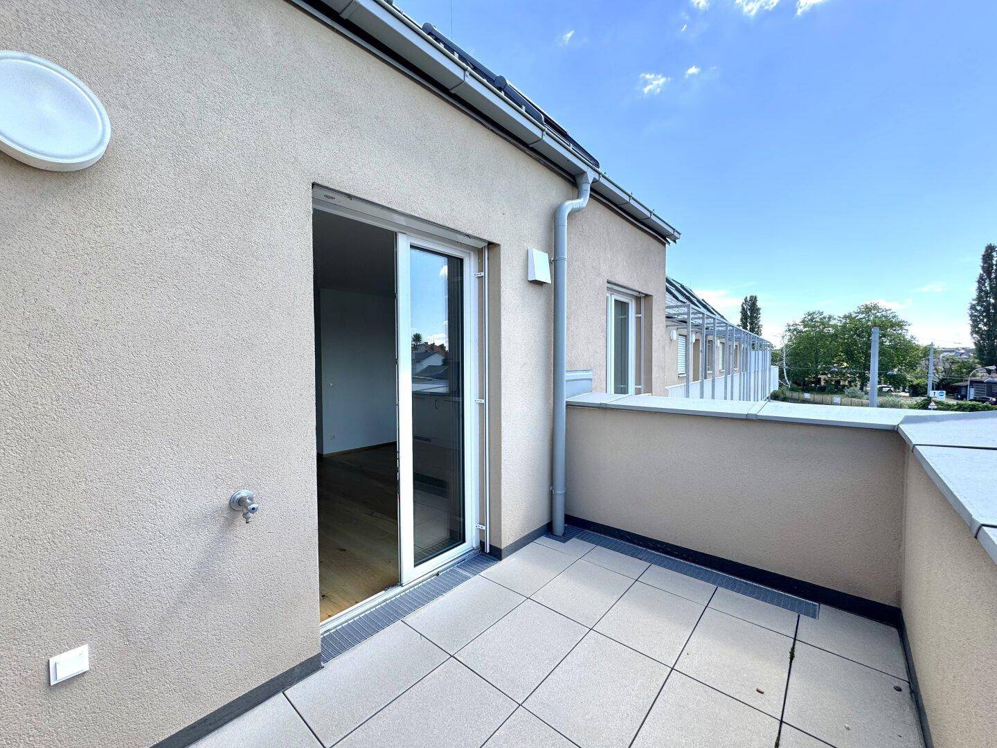 Helle Terrasse mit Fliesenboden und Zugang zu einem Innenraum, umgeben von moderner Architektur.