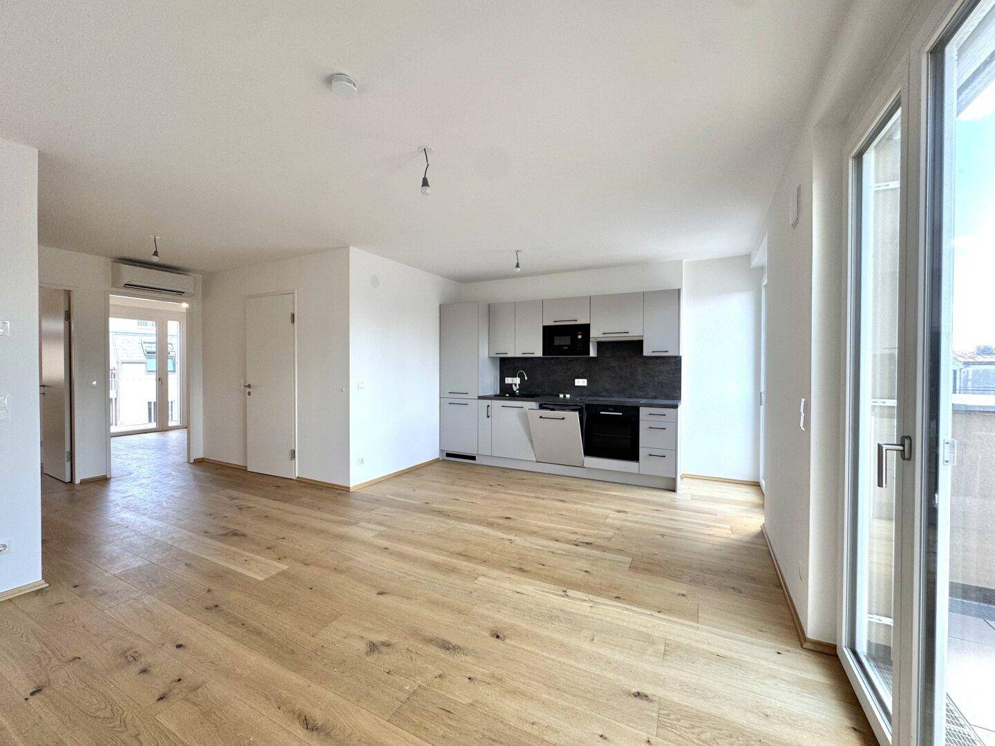 Heller Wohn- und Küchenbereich mit modernem Design, Holzboden und Zugang zu einem Außenbereich.