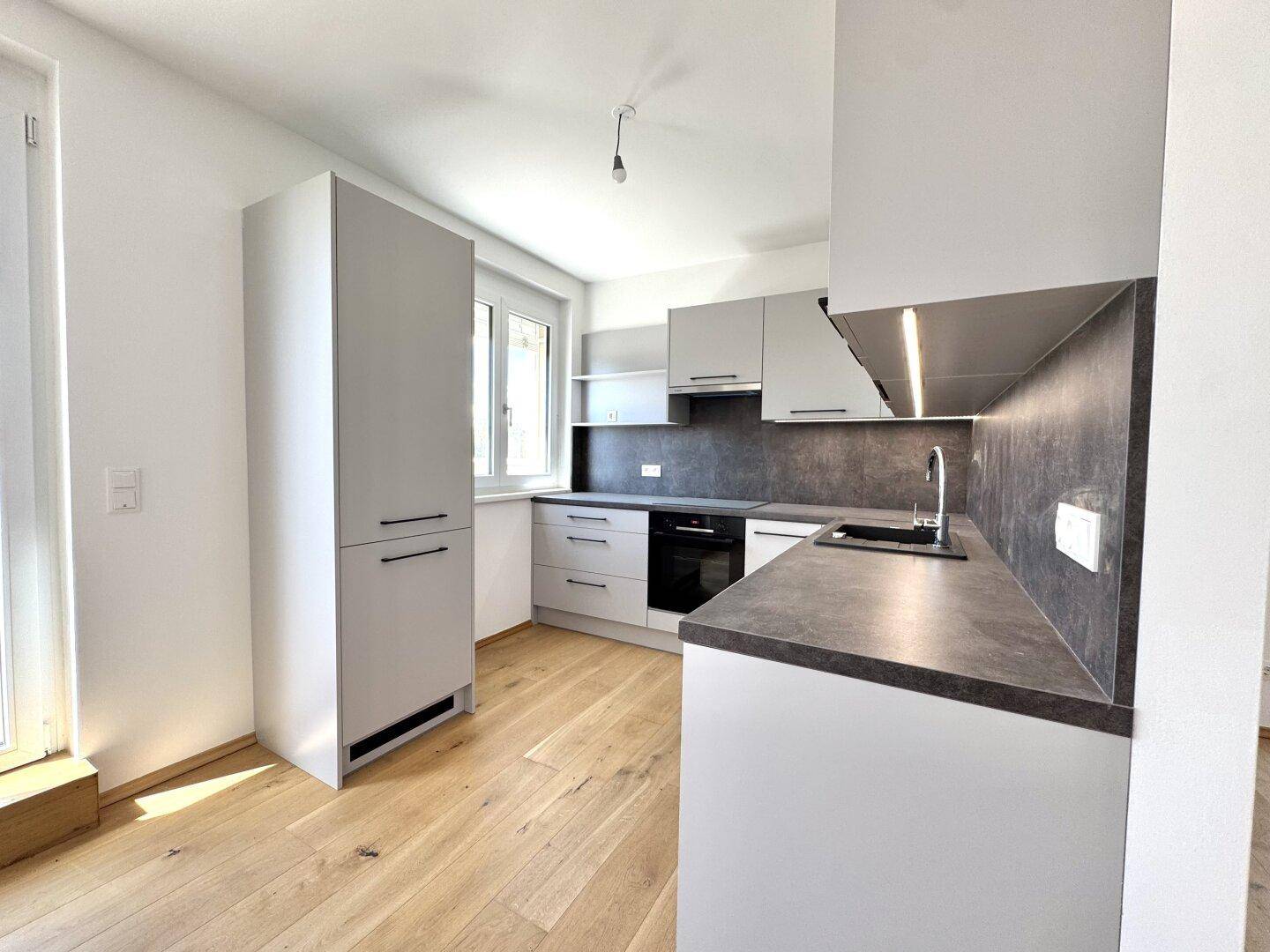 Helle Küche mit modernen grauen Schränken, dunkler Arbeitsplatte und Fenster für Tageslicht.