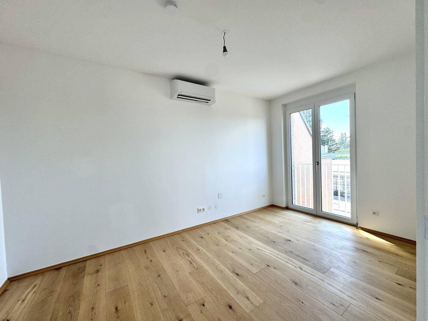 Helles Schlafzimmer mit Holzboden, Klimaanlage und Zugang zu einem kleinen Balkon.