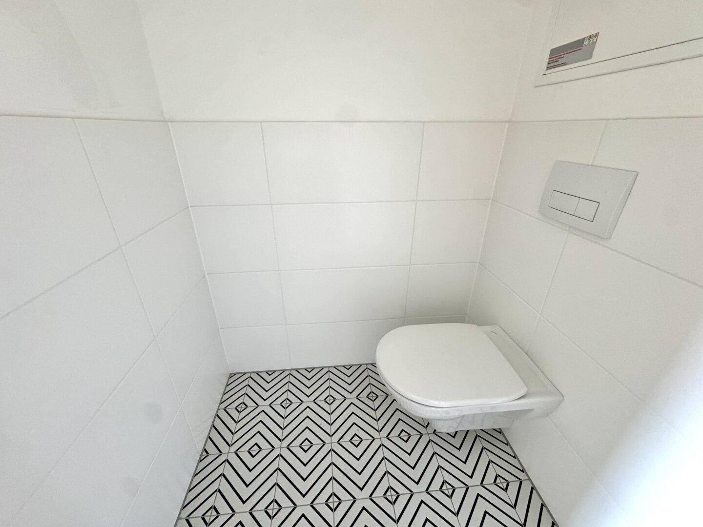 Modernes Gäste-WC mit weißen Fliesen und auffälligem schwarz-weiß gemustertem Fliesenboden.