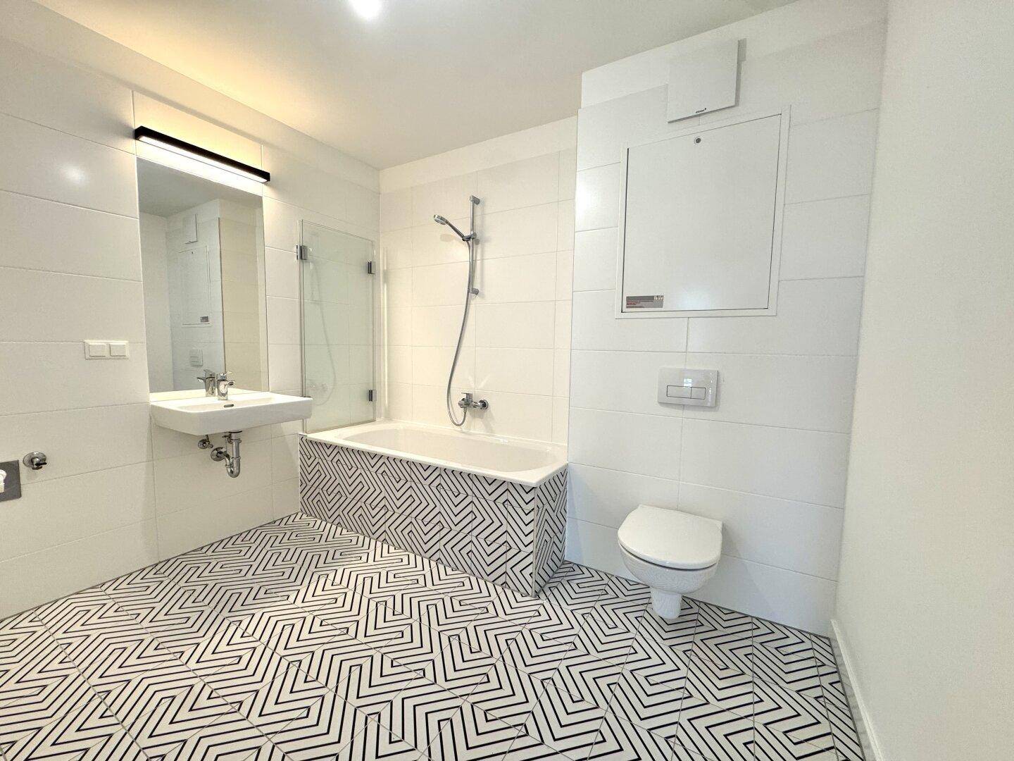 Modernes Badezimmer mit Badewanne, WC und auffälligen schwarz-weißen Fliesen.