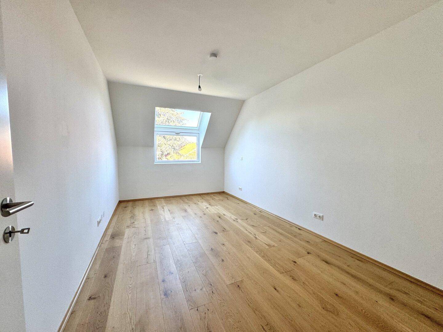 Dachgeschosszimmer mit Holzboden, weiß gestrichenen Wänden und Dachfenster.
