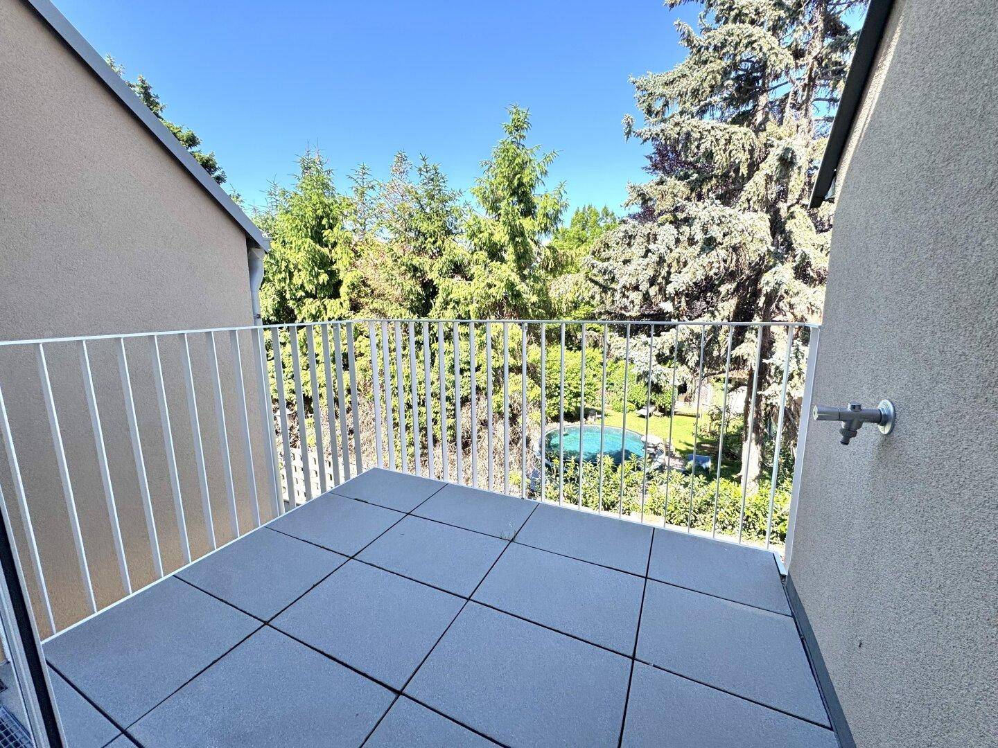 Heller Balkon mit Fliesenboden und Blick auf den grünen Gartenbereich mit Pool.
