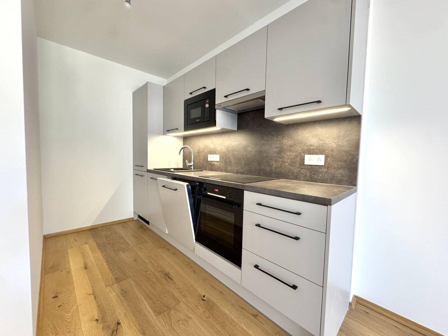 Moderne Einbauküche mit grauen Schränken, integrierten Geräten und Holzboden.