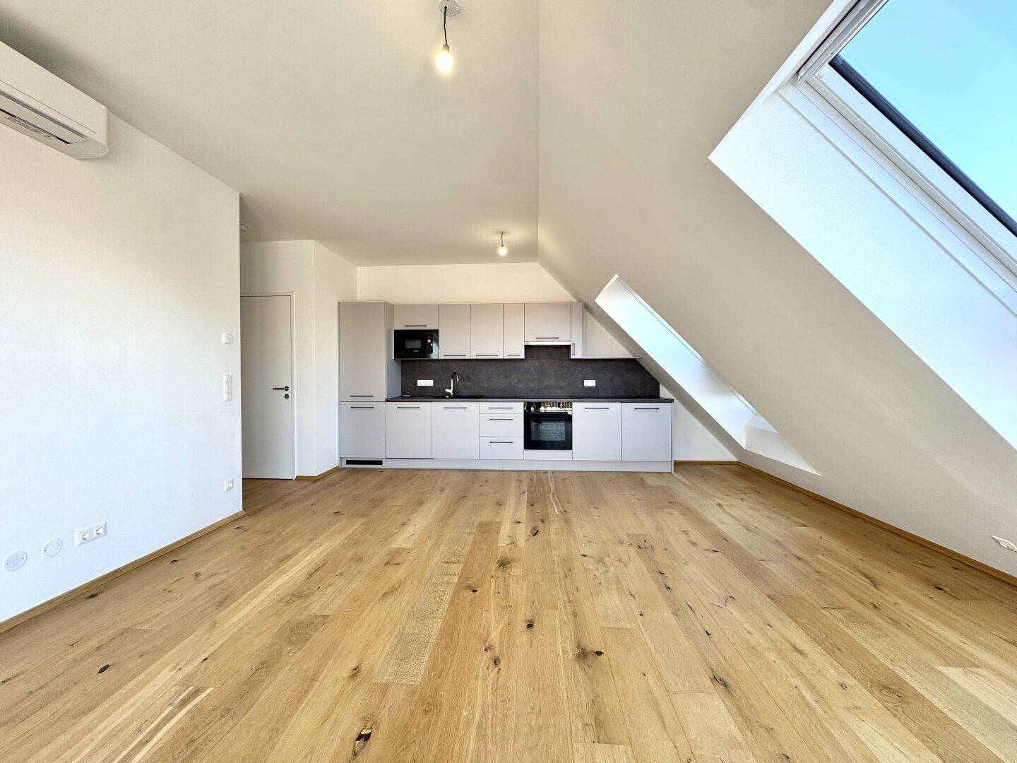 Offener Wohnbereich mit moderner Einbauküche, Holzboden und viel Tageslicht.