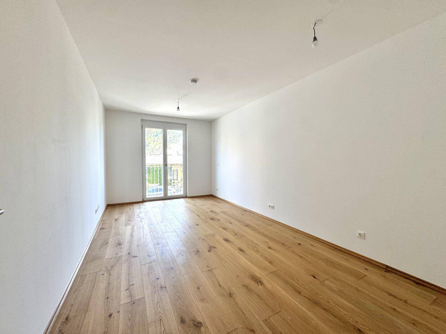 Geräumiges Zimmer mit hellem Holzparkett und Zugang zu einem französischen Balkon, ideal als Schlafzimmer.
