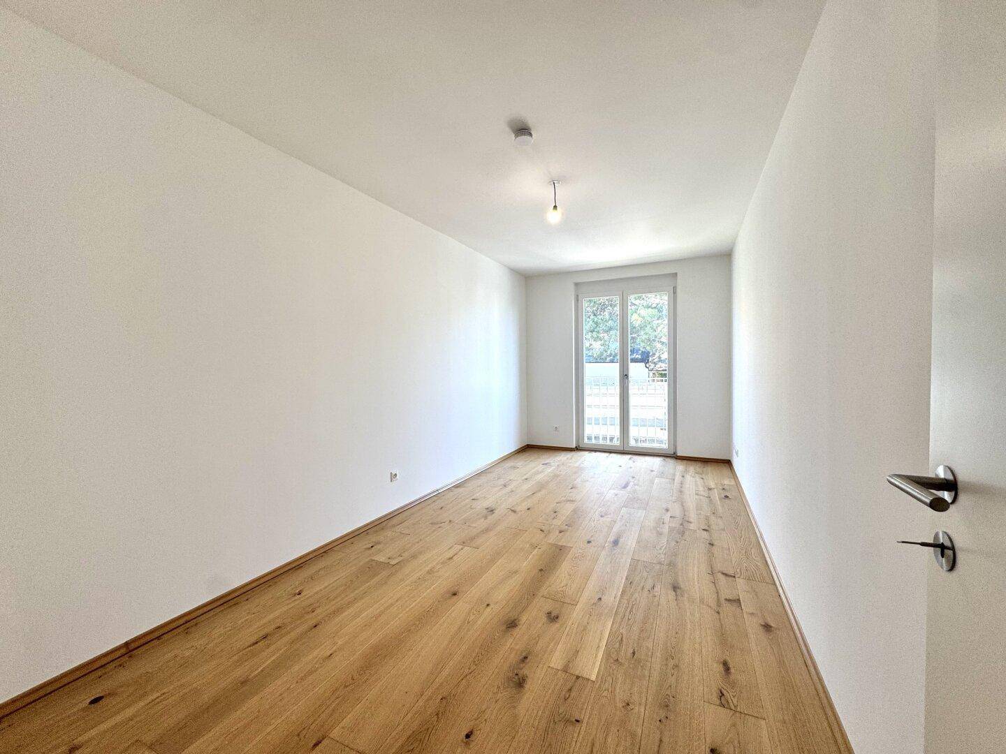 Helles Schlafzimmer mit Holzfußboden und einem französischen Balkon, der viel Tageslicht hereinlässt.