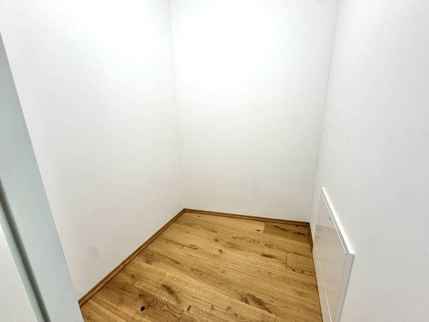 Kleiner Abstellraum mit Holzfußboden und weißen Wänden, ideal für zusätzlichen Stauraum.