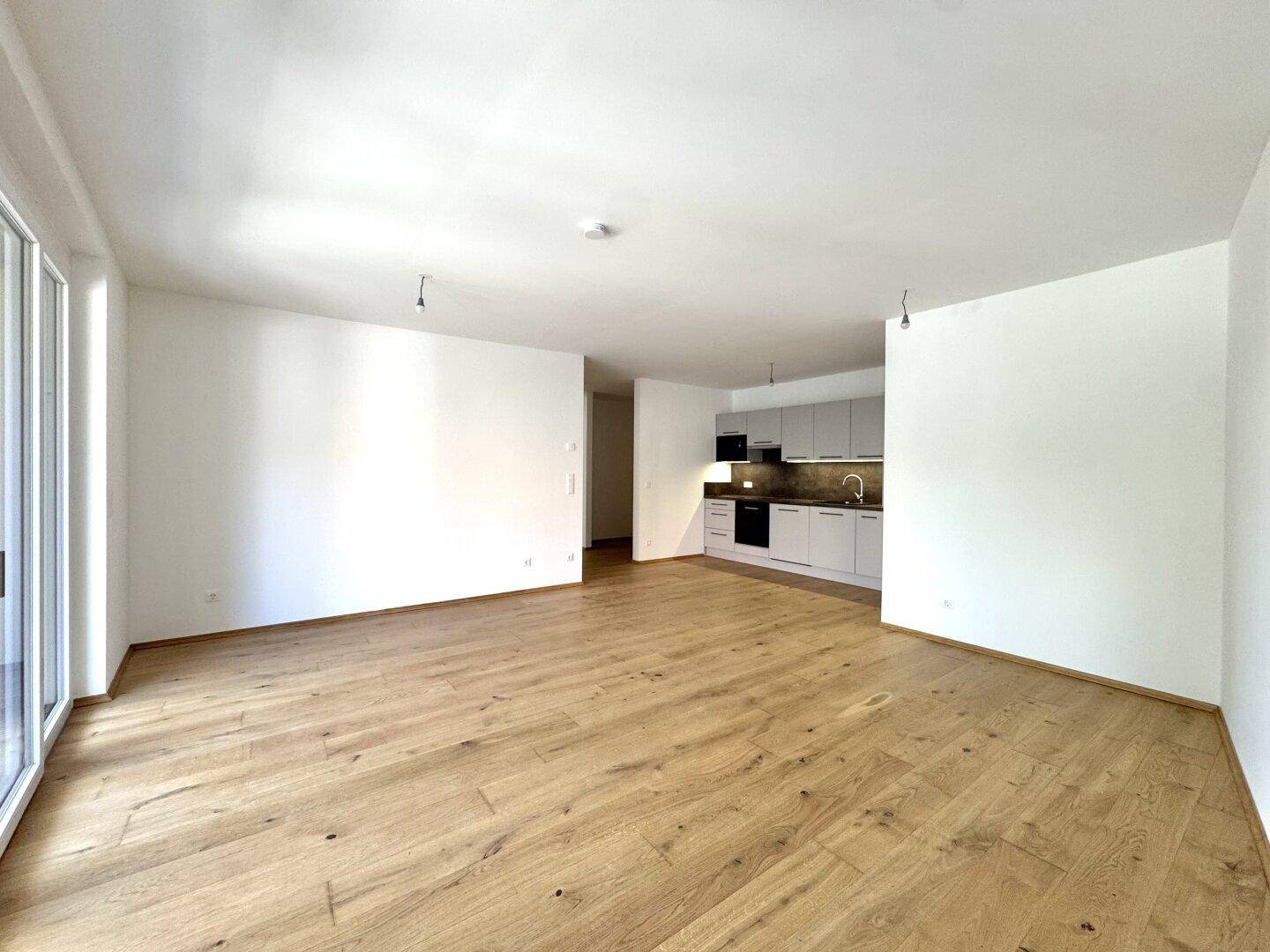 Heller, offener Wohnbereich mit integrierter Küche und Zugang zu einem Balkon oder einer Terrasse.