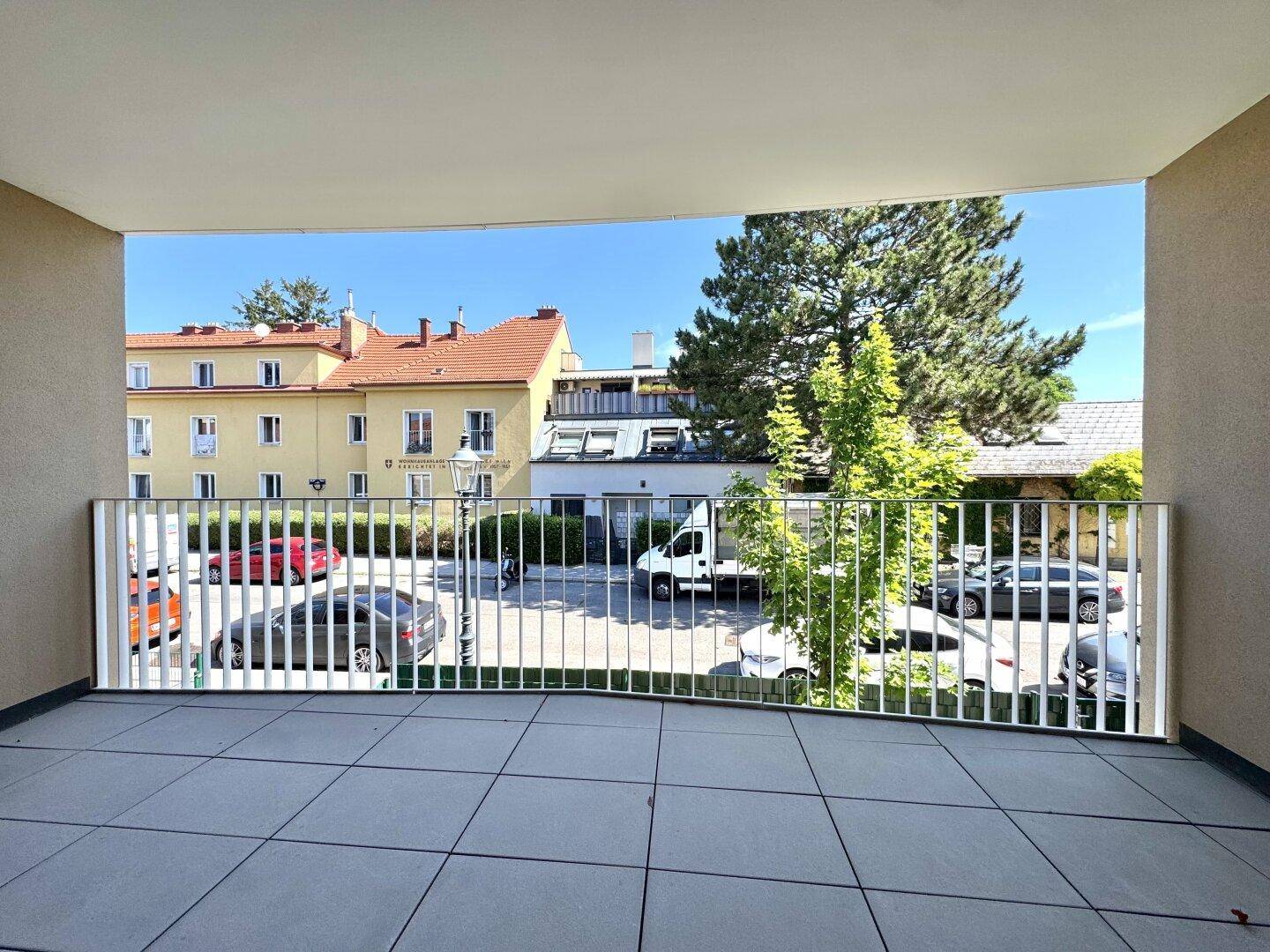 Geräumiger Balkon mit Fliesenboden und Blick auf die umliegenden Gebäude und Bäume.