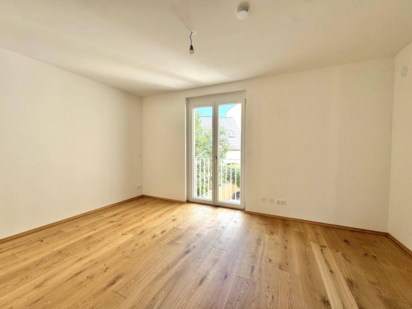 Helles Schlafzimmer mit Holzparkettboden und einem französischen Balkon für viel Tageslicht.