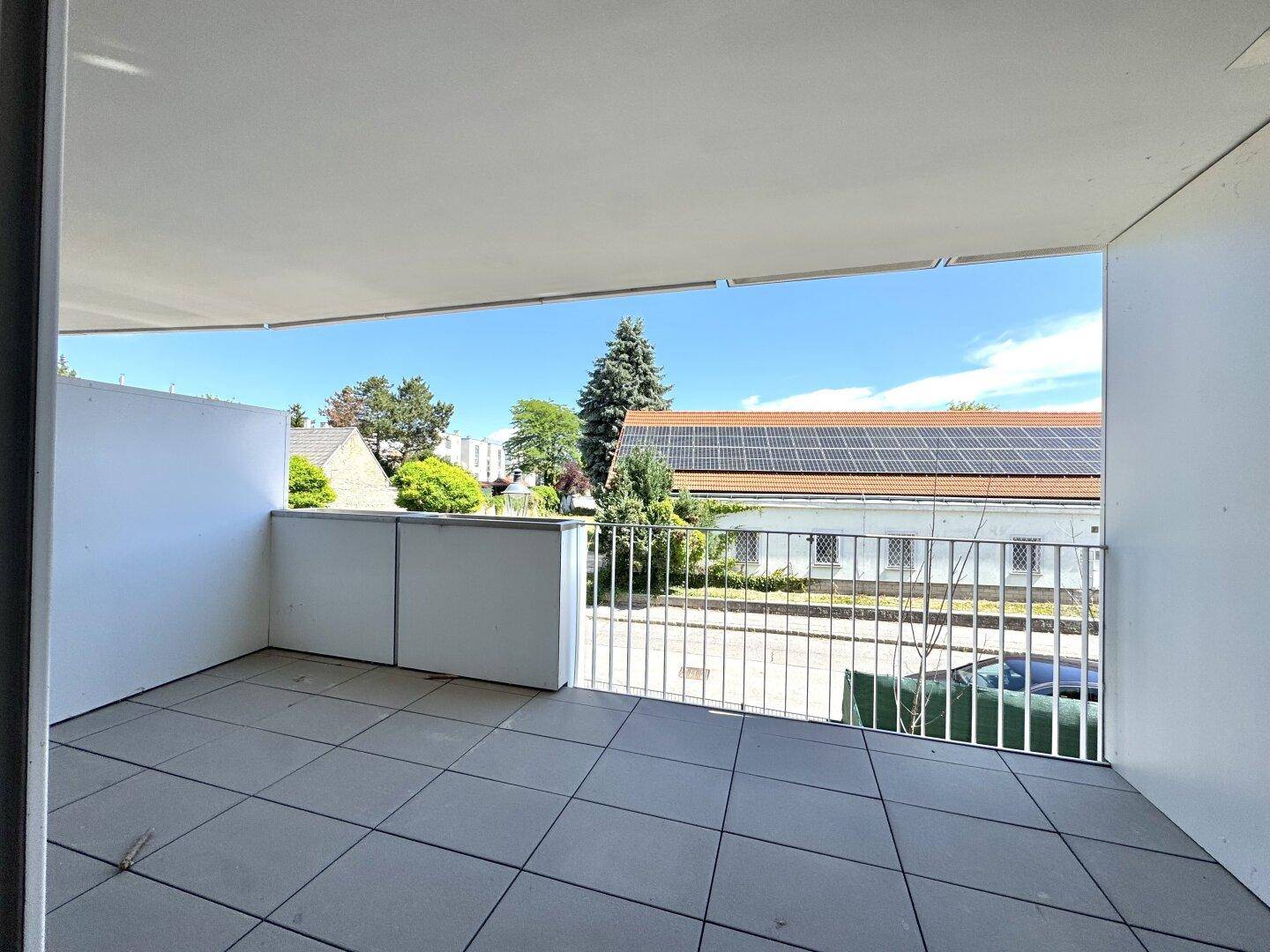 Geräumiger Balkon mit Fliesenboden und weitem Blick auf die Umgebung und den blauen Himmel.