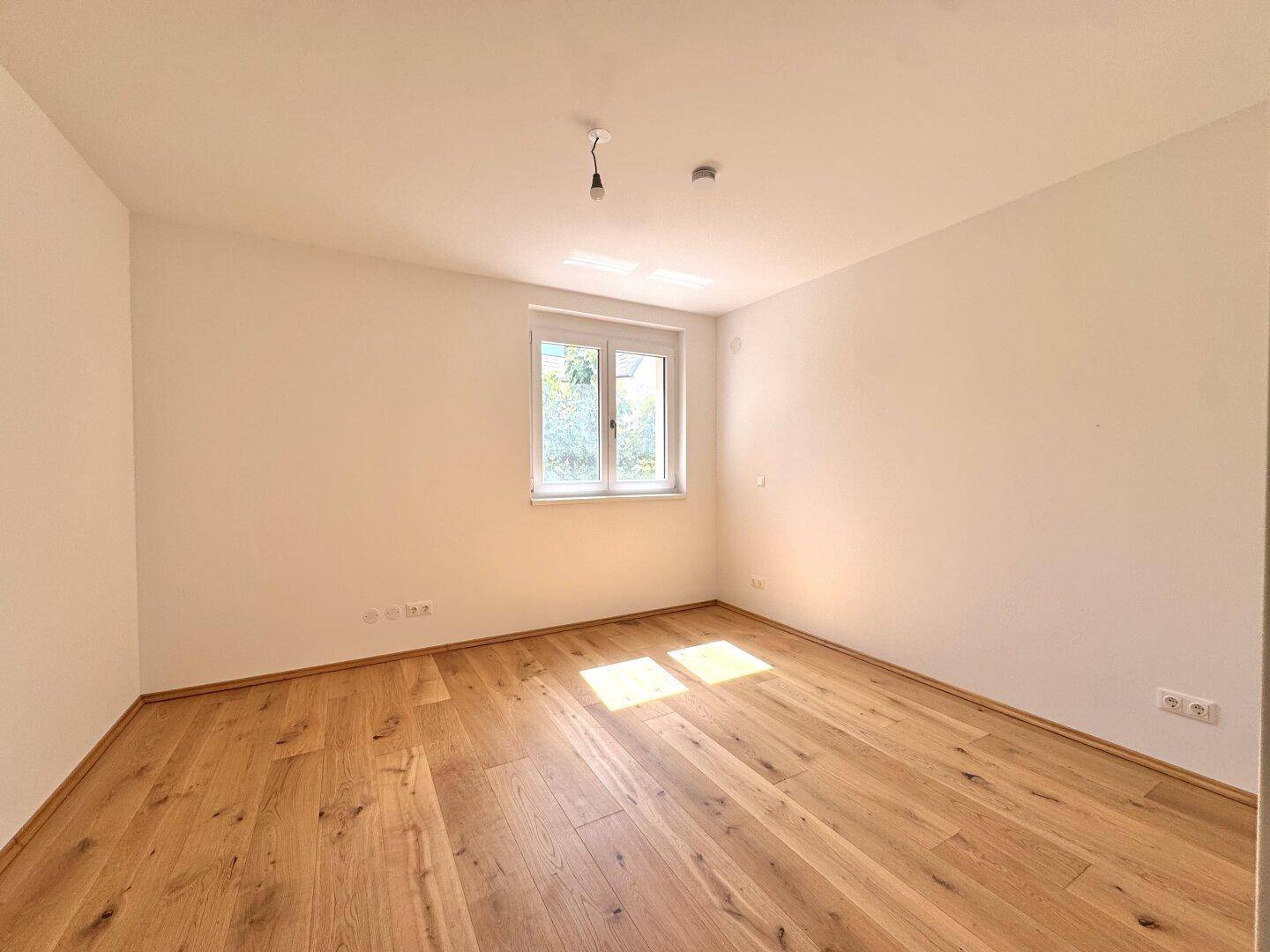 Helles Schlafzimmer mit Holzboden und einem Fenster, das für natürliche Belichtung sorgt.