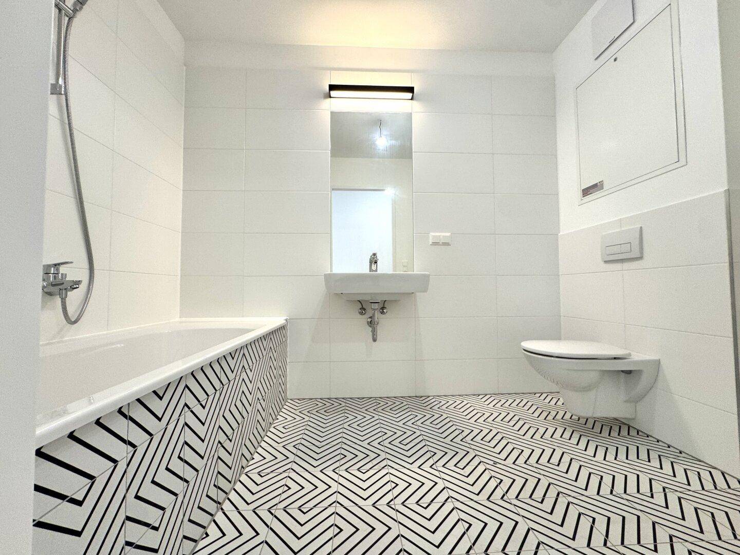Modernes Badezimmer mit Badewanne, Wand-WC und auffälligen schwarz-weißen Fliesen am Boden.