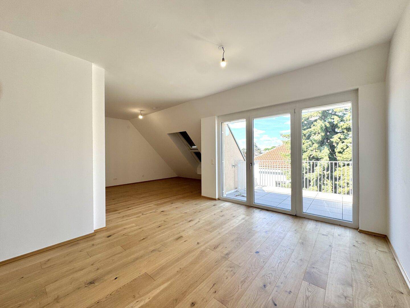 Geräumiger, heller Raum mit Holzboden und Zugang zu einem Balkon, ideal als Wohnbereich.
