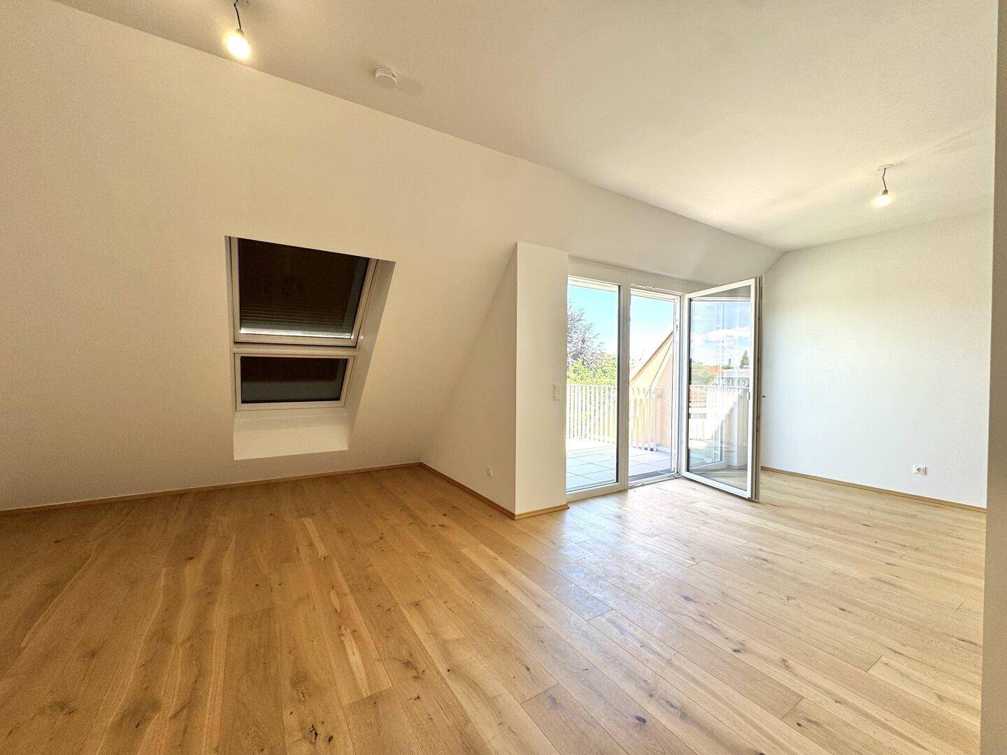 Heller Raum mit Holzboden, Dachfenster und Balkonzugang, bietet viel natürliches Licht.