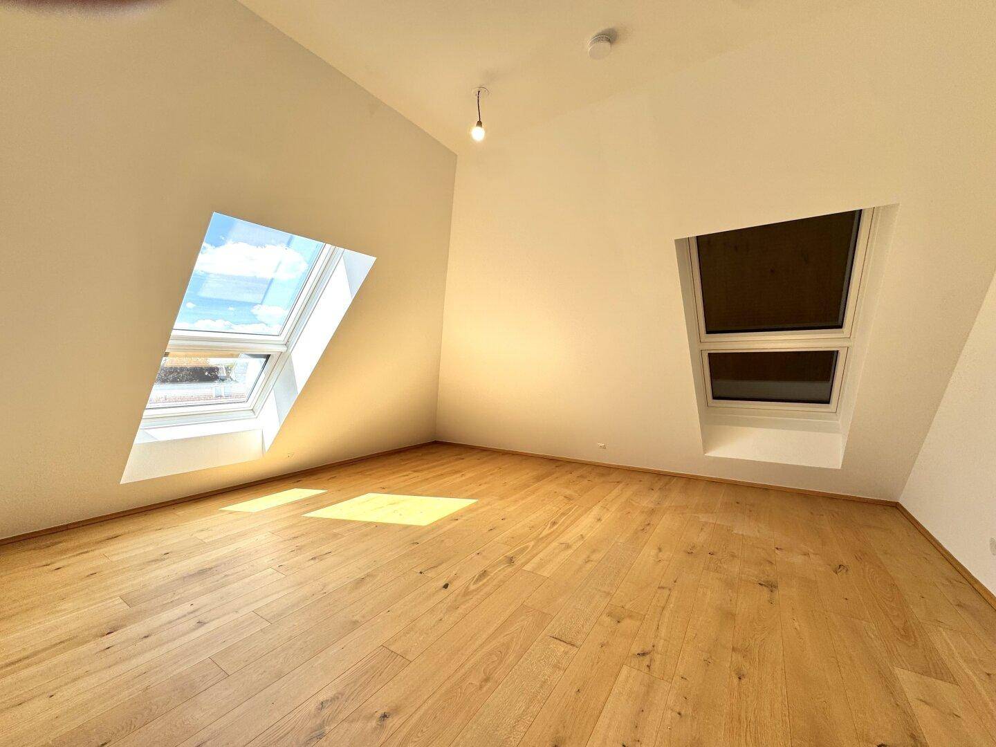 Helles Schlafzimmer mit Holzboden und zwei Dachfenstern, bietet eine gemütliche Atmosphäre.